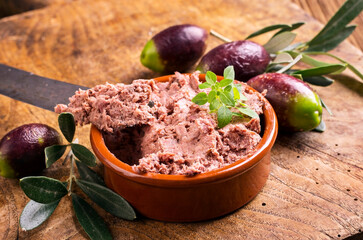 Traditional French goose pate as spread in a bowl with  olives served as close-up on a rustic...