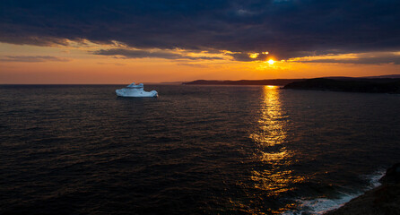 Obraz premium Newfoundland iceberg golden sunset landscape scene with streaming sunset light reflections in water, outdoor evening ocean view.
