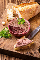 Traditional French goose pate as spread in a bowl with baguette and olives served as close-up on a...