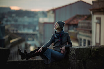 A woman sits on an stone wall at dusk in Porto downtown, Portugal.