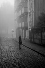 A woman enjoys the atmosphere on a deserted street in the thick fall morning fog. Black and white photo.