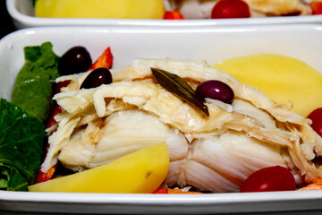 Real Portuguese codfish recipe in slices with potatoes, black olives and cabbage in selective focus