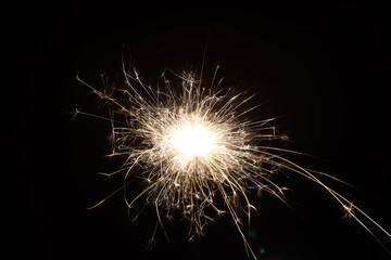 A single sparkler illuminates the darkness, its brilliant light shining like a star against the black background, the festive sparkler symbolizes joy and celebration.