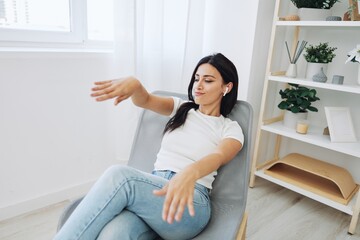Woman sitting in chair listening to music on wireless headphones at home, fall lifestyle