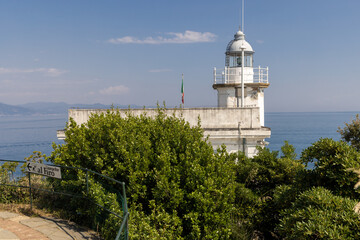 Fototapeta na wymiar Faro (Lighthouse) of Portofino with outdoor cafe, bar with a sea view. Portofino is a fishing village on the Italian Riviera coastline, region of Liguria, Italy. May 10, 2022