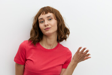 Fototapeta na wymiar a sweet, pleasant, thoughtful woman stands on a white background and looks into the camera gesturing with her hand. Horizontal photo with an empty space for inserting an advertising layout