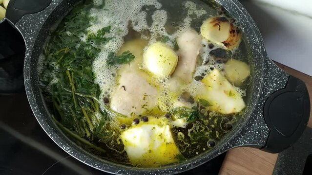 Chicken broth with vegetables and spices cooking in a pot on the stove. Homemade dinner preparation