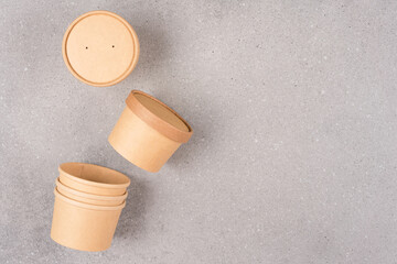 Brown disposable kraft paper food containers for soup or ice cream, cup with paper cap over gray concrete table background with copy space, mockup image. Sustainable food packaging concept