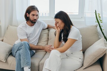 A man and a woman of different races sit on the couch in a room at home and talk about their problems to each other. A stress-free lifestyle of family quarrels with psychological support