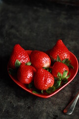 Strawberries on the heart-shaped plate in the dark background. Fresh red fruit