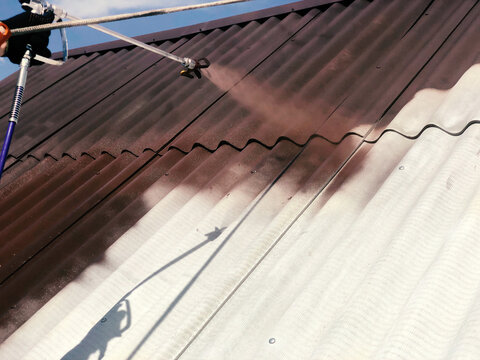 Roofer painting a slate sheet roof brown with a high pressure sprayer