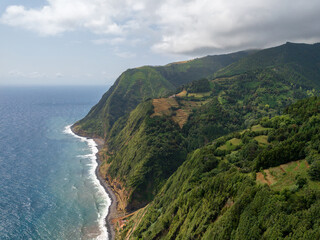 Fototapeta na wymiar Amazing landscape on the northeast coast of the island of Sao Miguel in the Azores. Panoramic view of cliff with a path to the sea and a small fishing port. Tourist attraction of Portugal.
