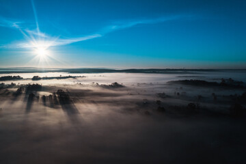 Fototapeta na wymiar Flying over a village at dawn, bright sun on the horizon and fog over a small village.