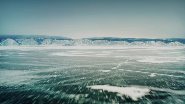 Fast flight over the ice of Lake Baikal, with a mountain range in the background. Olkhon Island, the Little Sea Strait. Baikal, Siberia, Russia. Drone aerial shot 4k