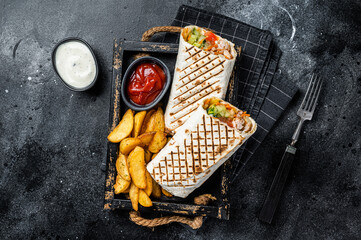 Durum doner kebab or Shawarma with meat, vegetable salad and french fries. Black background. Top...