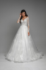 Full length bride portrait. Elegant woman in white wedding dress standing in grey interior.Attractive female model standing and posing in ball gown.
