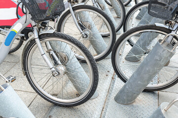 Obraz premium Bicycles on the street in the city for rental. Urban background. Rental of bikes. A row of gray bikes with baskets available to sell or rent. 