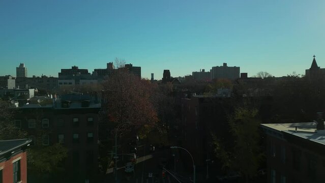 Forwards fly above street at roof level. Buildings and autumn trees in large city. New York City, USA