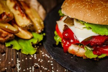 Closeup juicy burger with french fries, ketchup, fresh vegetables on stone board. Homemade cooking
