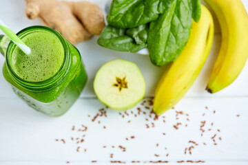 From above shot of mason jar mug filled with green smoothie and ingredients on wooden table. 