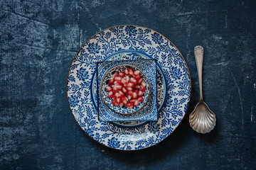 Red ripe pomegranate seeds, pieces with skin and membranes of cuted fruit on glazed ceramic blue Middle eastern or arabic oriental dishes. Healthy vegan, vegetarian food. Blue background. Top view