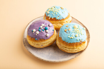 Purple and blue glazed donut on orange pastel, side view.
