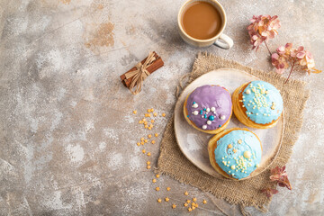 Fototapeta premium Purple and blue glazed donut and cup of coffee on brown concrete, top view, copy space.