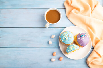 Purple and blue glazed donut and cup of coffee on blue wooden, top view, copy space.