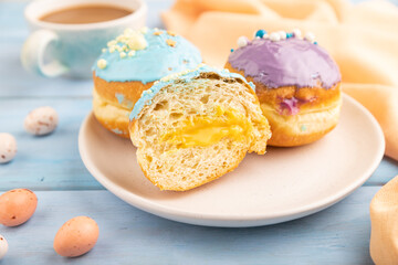 Purple and blue glazed donut and cup of coffee on blue wooden, side view, selective focus.