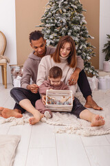 A family is sitting on a knitted blanket, holding a wooden box with Christmas toys.