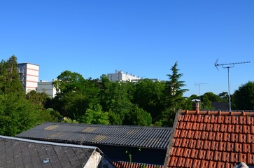 Urban landscape: view of tiled roofs, corrugated iron roofs, slate roofs, TV antennas, trees and buildings in the background, perspective view.