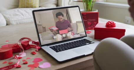 Happy african american man opening gift and making valentine's day video call on laptop