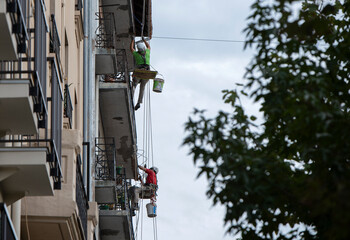painters working on facade hanging from ropes