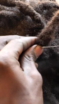 Vertical video of close shot of black hands tiddying dreadlocks at the base while smoking