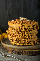 A stack of paleo pumpkin waffkes in a plate and wook trivet with butter and pecans - 557776100