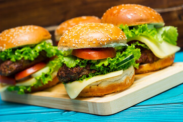 Homemade hamburgers with meat, cheese, lettuce, tomato on a wooden table