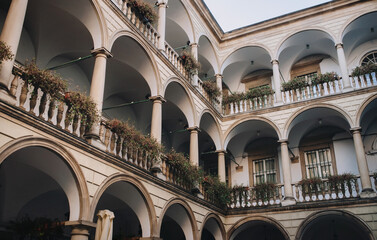 Old european Renaissance three-story arcade, roses and other flowers in hanging pots on the balconies. Ancient architecture of Lviv, Ukraine. View of the patio from below. © shchus