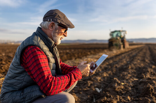 Senior farmer with tablet in field with tractor in background