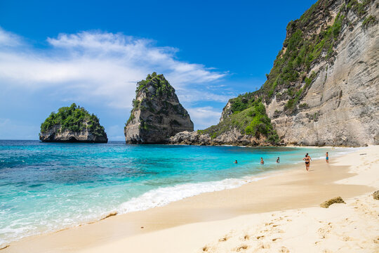 BALI / INDONESIA - NOVEMBER 8, 2022: People swimming at the beautiful sandy beach (Diamond beach) with rocky mountains and clear water in Nusa Penida.