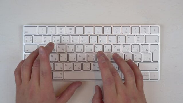 A man is typing on a white wireless keyboard.