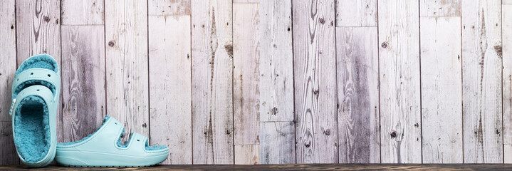 blue rubber sandals with faux fur inside stand against a wall of gray planks. Banner. Space for text.