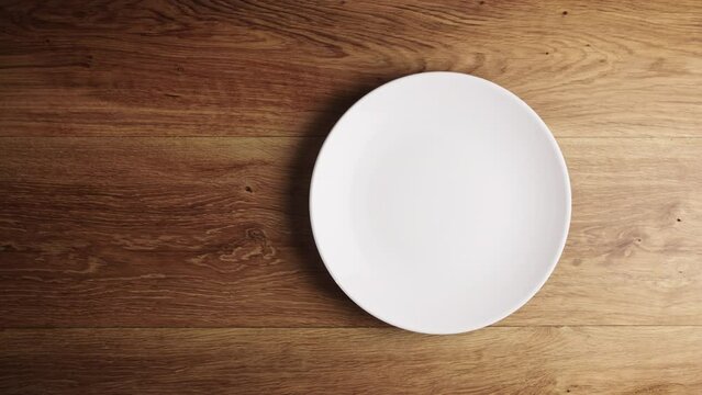 High angle shot of a male hand placing an empty white plate on a wooden table. Dieting, cooking and food concept.