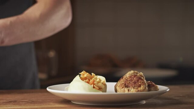 Male home chef plating a dish with Bulgarian potato patties and a cabbage and carrot salad.