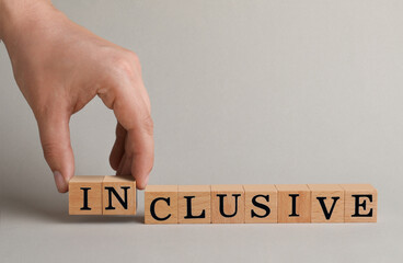 Woman making word Inclusive with wooden cubes on beige background, closeup. Space for text