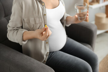 Pregnant woman holding pill and glass with water indoors, closeup