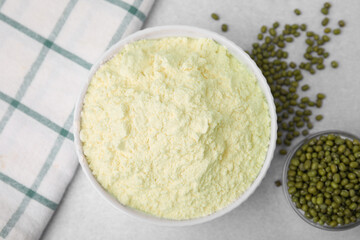 Mung bean flour in bowl and seeds on white table, flat lay