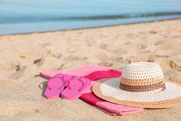 Beach towel with straw hat and slippers on sand near sea
