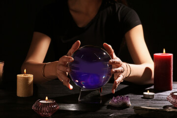 Soothsayer using crystal ball to predict future at table in darkness, closeup