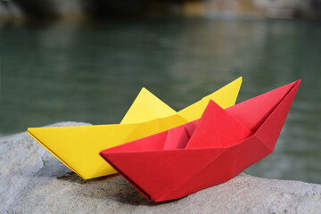 Beautiful yellow and red paper boats on stone near water outdoors, closeup