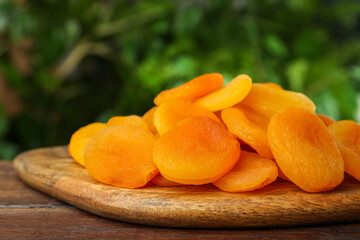 Tasty apricots on wooden table against blurred green background. Dried fruits